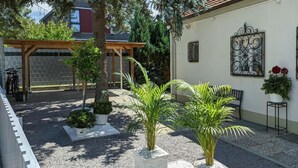 Une cour agrémentée de plantes en pot, une pergola et un bâtiment doté d’un toit en tuiles.
