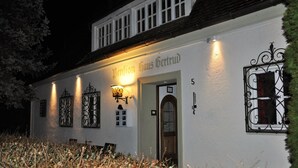 Un bâtiment blanc portant l’inscription « Verein Haus Gertrud », illuminée la nuit.
