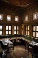 A room with a long dining table set for a meal, surrounded by chairs, with a patterned carpet and a chandelier.