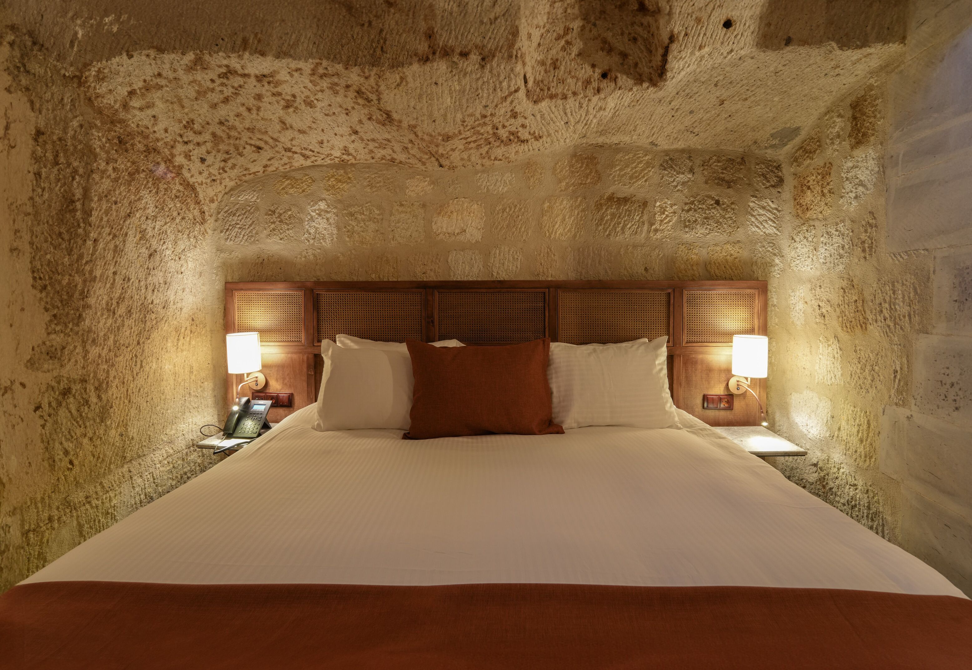 A large bed with a wooden headboard, two bedside lamps, and a telephone on the left side.