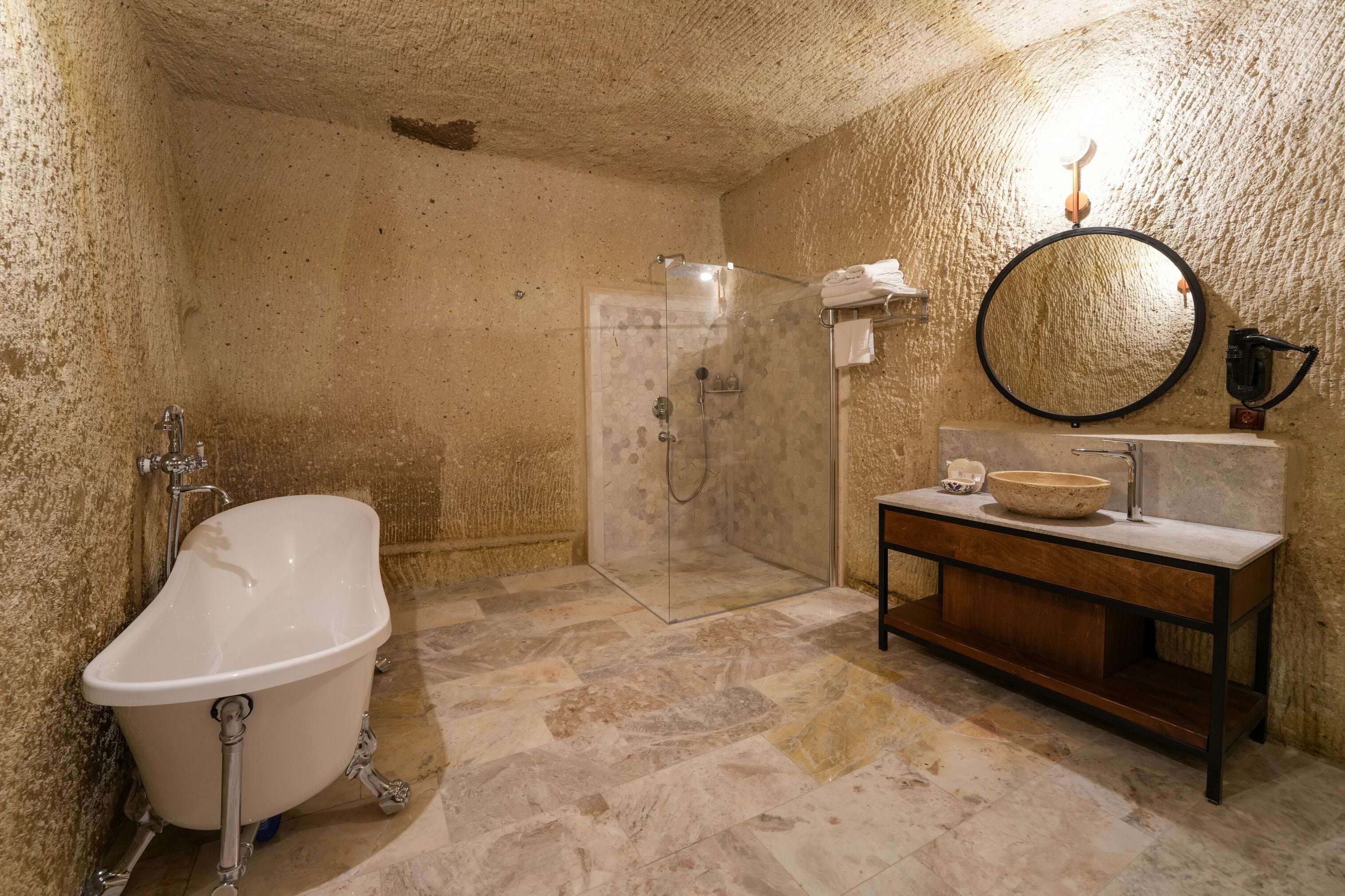 A bathroom with a freestanding bathtub, a glass-enclosed shower, and a wooden vanity with a round mirror.