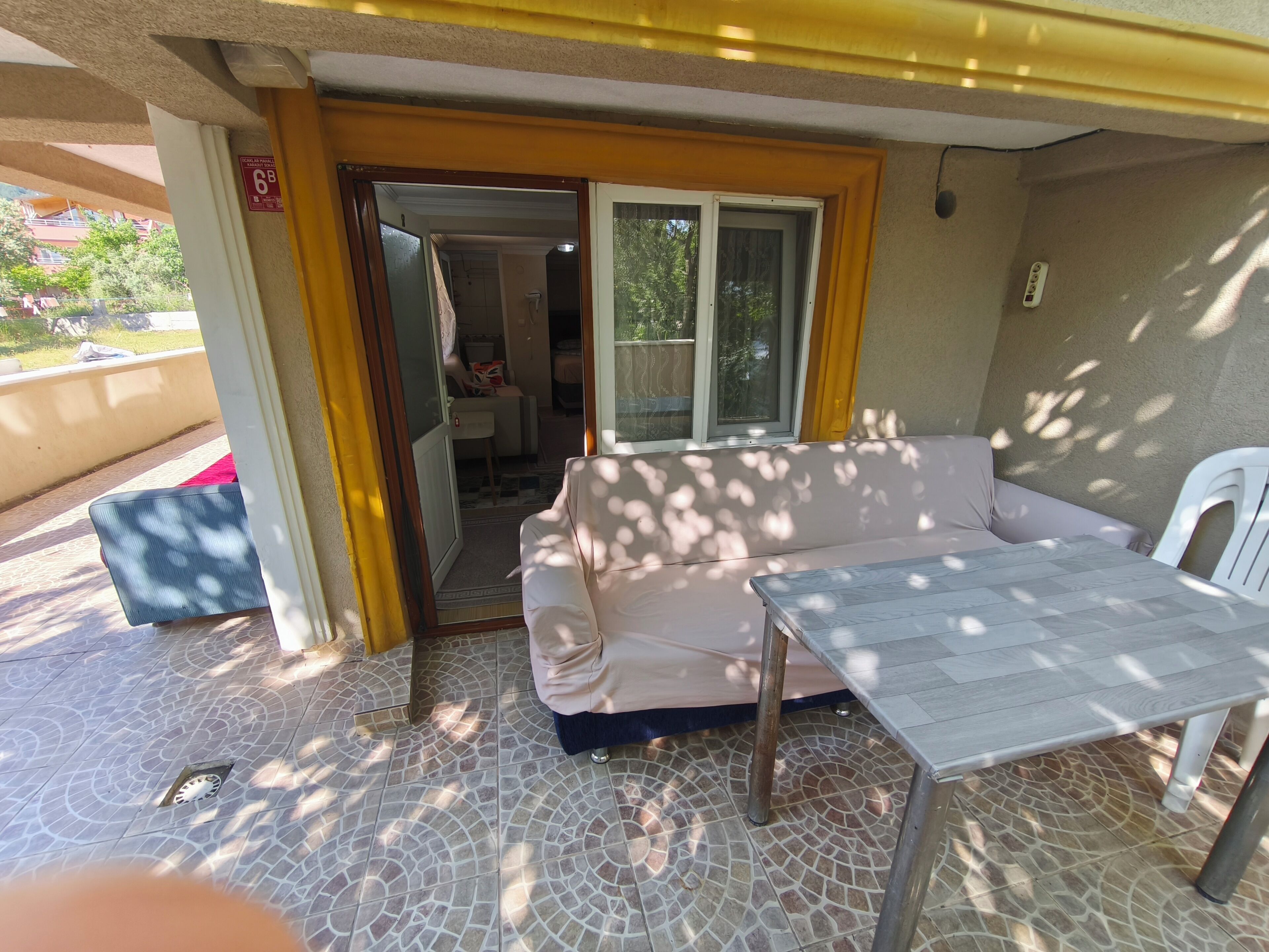 An outdoor patio area with a white sofa, a table, and a chair. There is a door leading to an interior space.