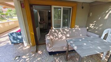 An outdoor patio area with a white sofa, a table, and a chair. There is a door leading to an interior space.