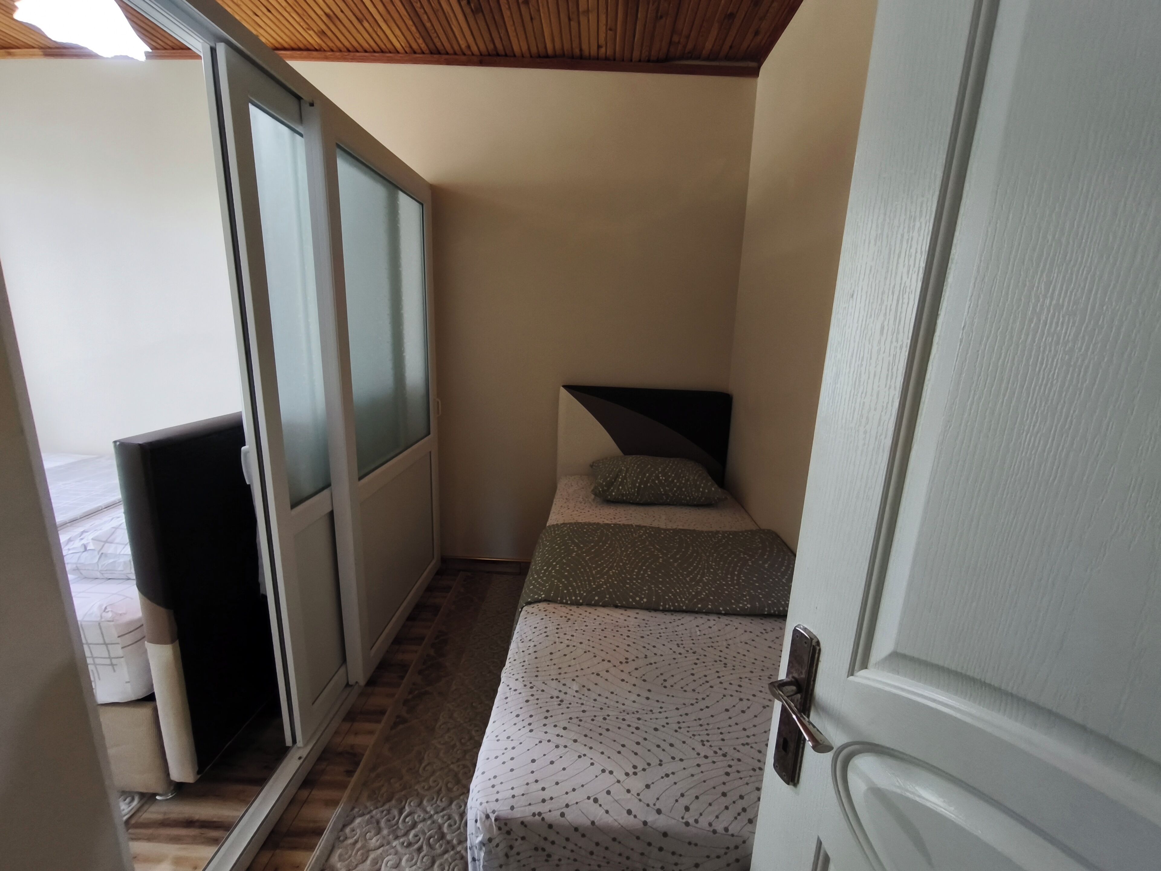 A narrow room with a bed, a door, and a window.