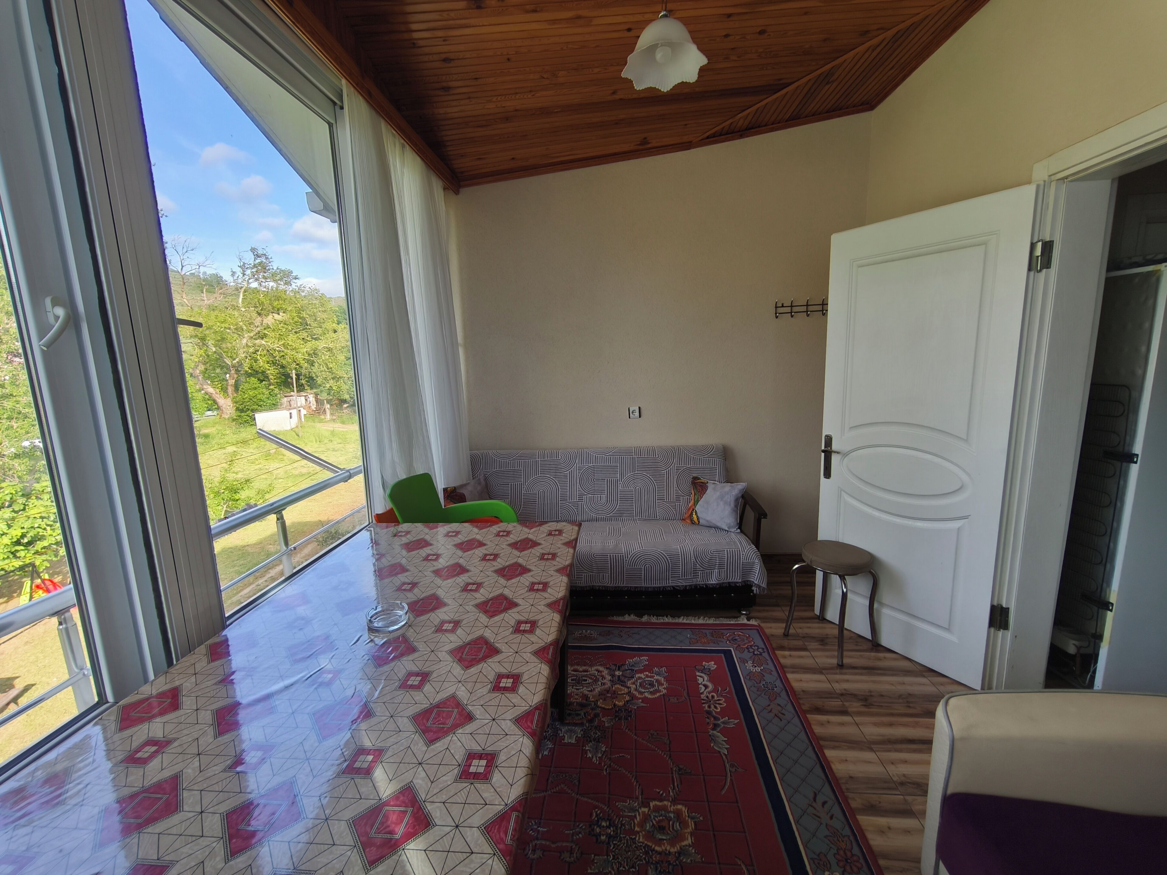 A room with a large window, a sofa, a chair, a patterned rug, and a door.
