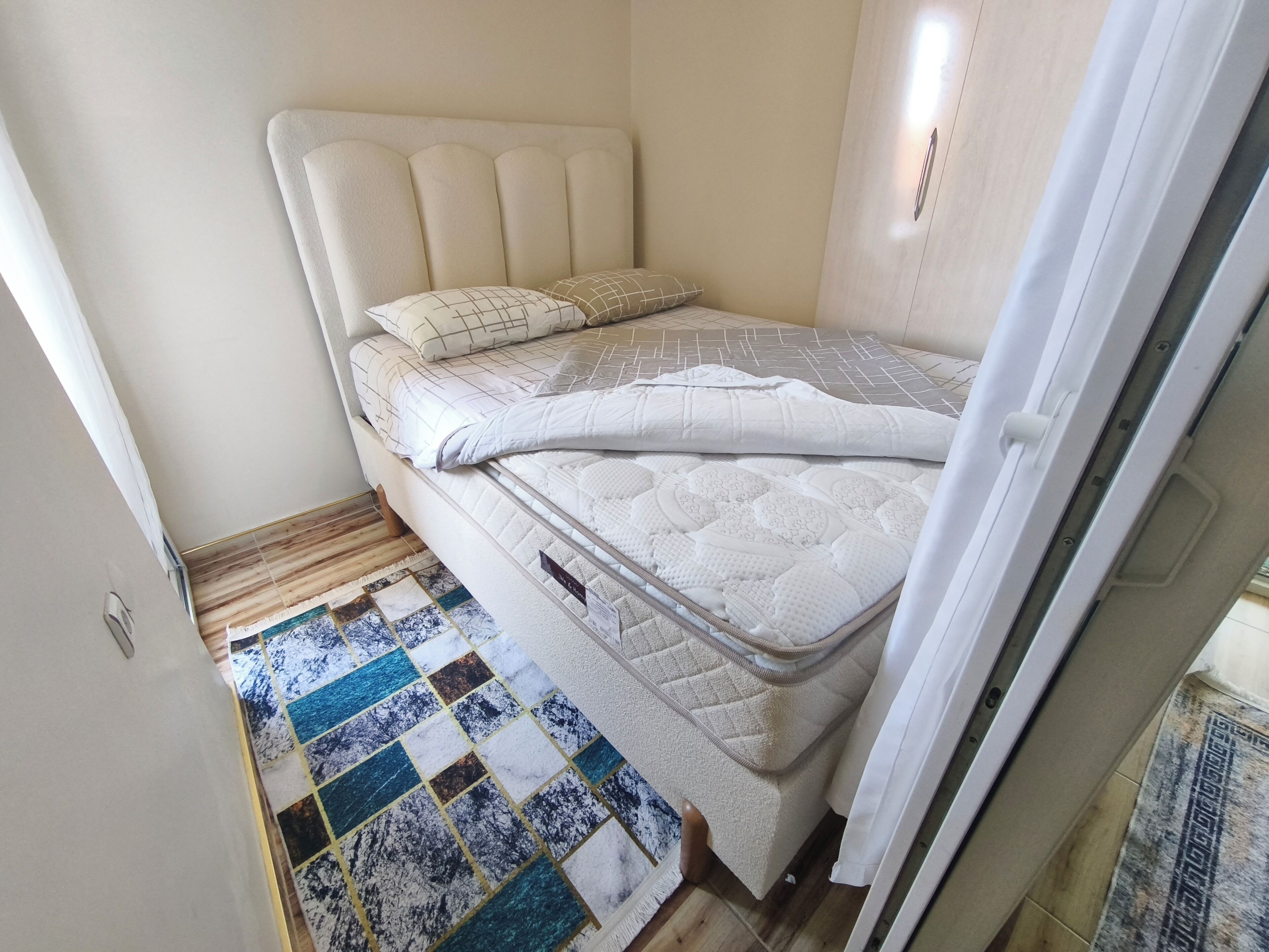 A single bed with a headboard, a quilted mattress, and a patterned rug.