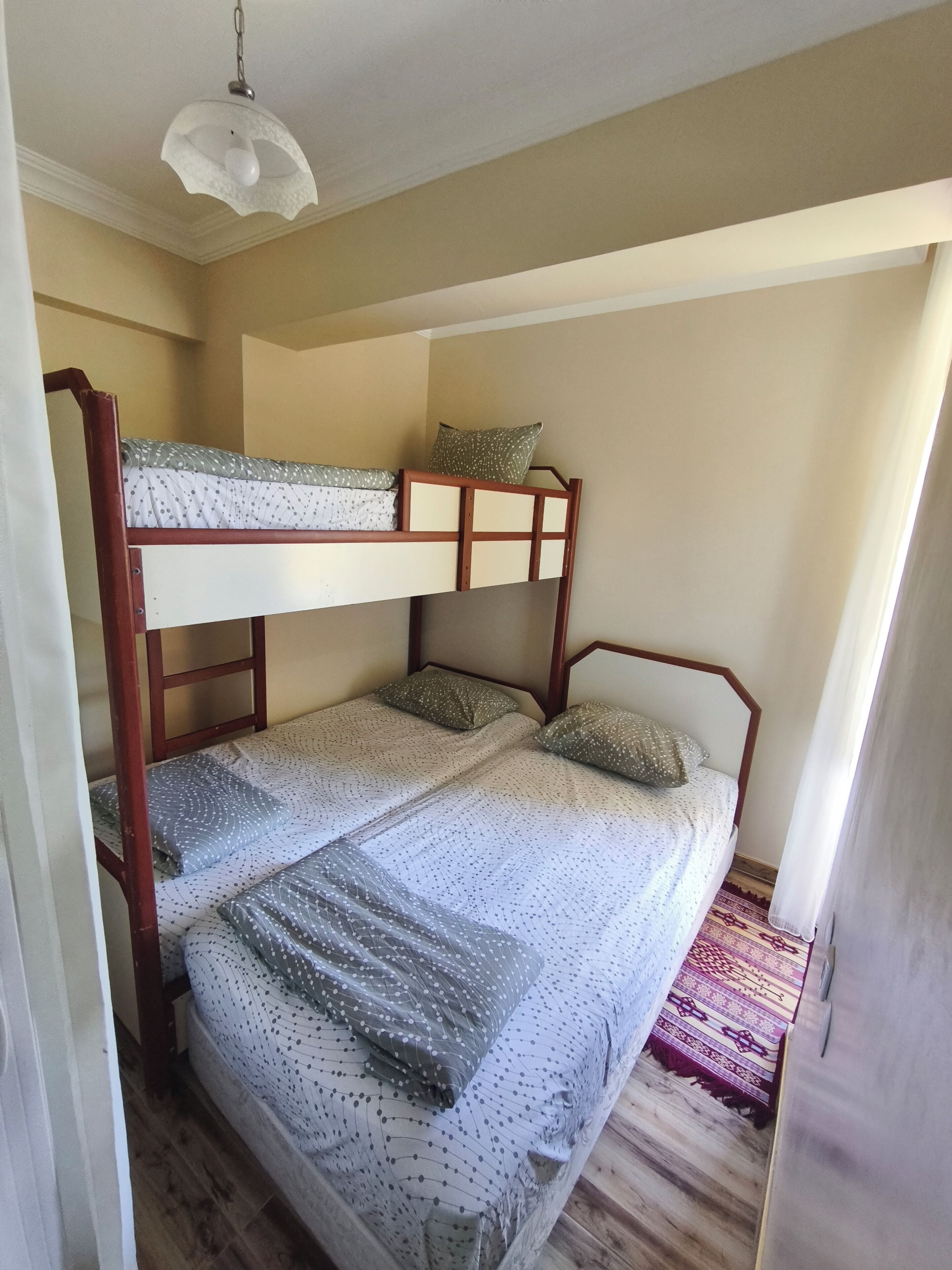A bunk bed room with a patterned bedspread, a hanging light fixture, and a patterned rug.
