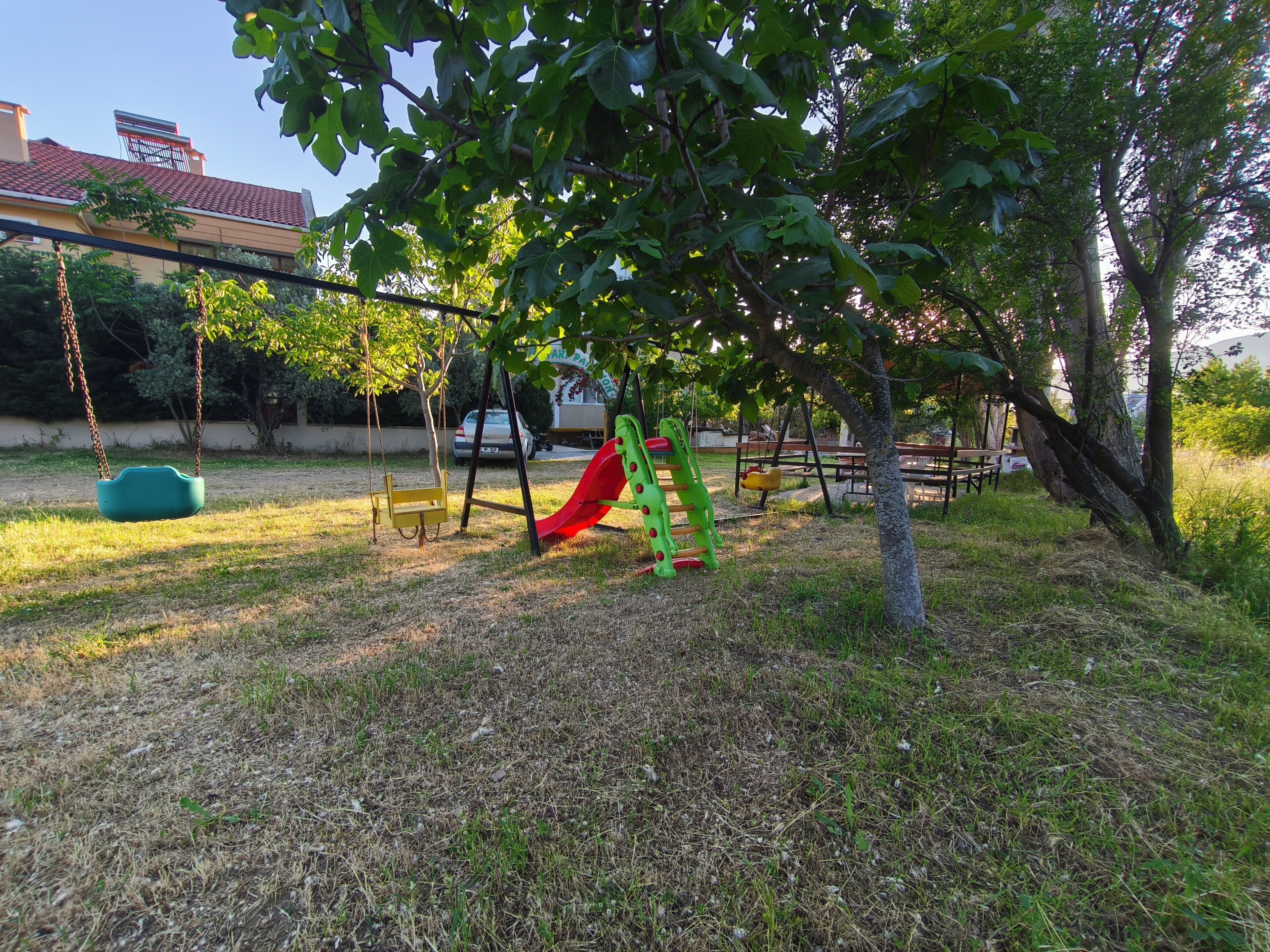 Un parque infantil con columpios y un tobogán, rodeado de árboles y césped.