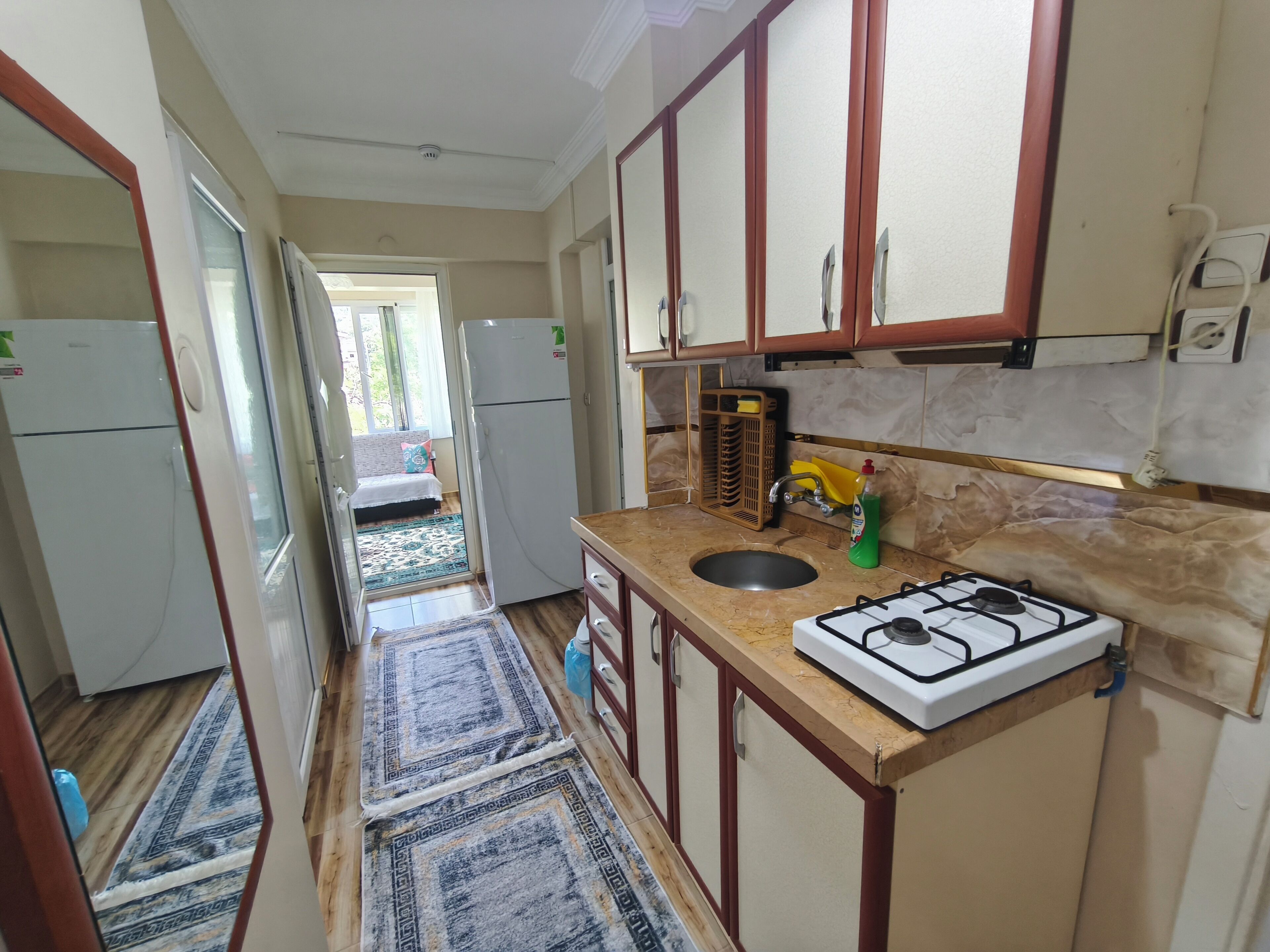 Une cuisine étroite avec une cuisinière à gaz, un évier et des armoires en bois.