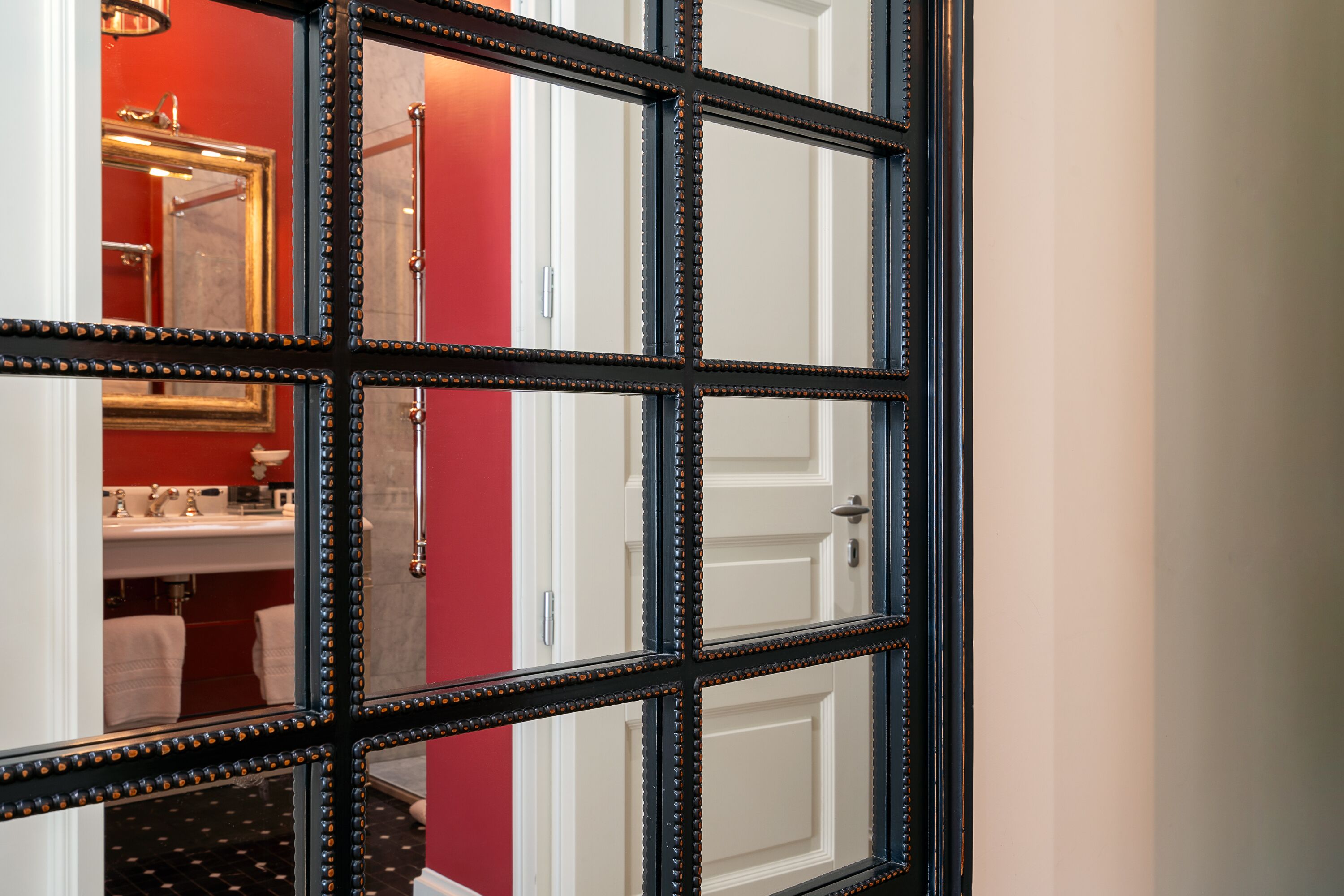 Une salle de bain avec un mur rouge, une porte blanche et un miroir doté d’un cadre noir.