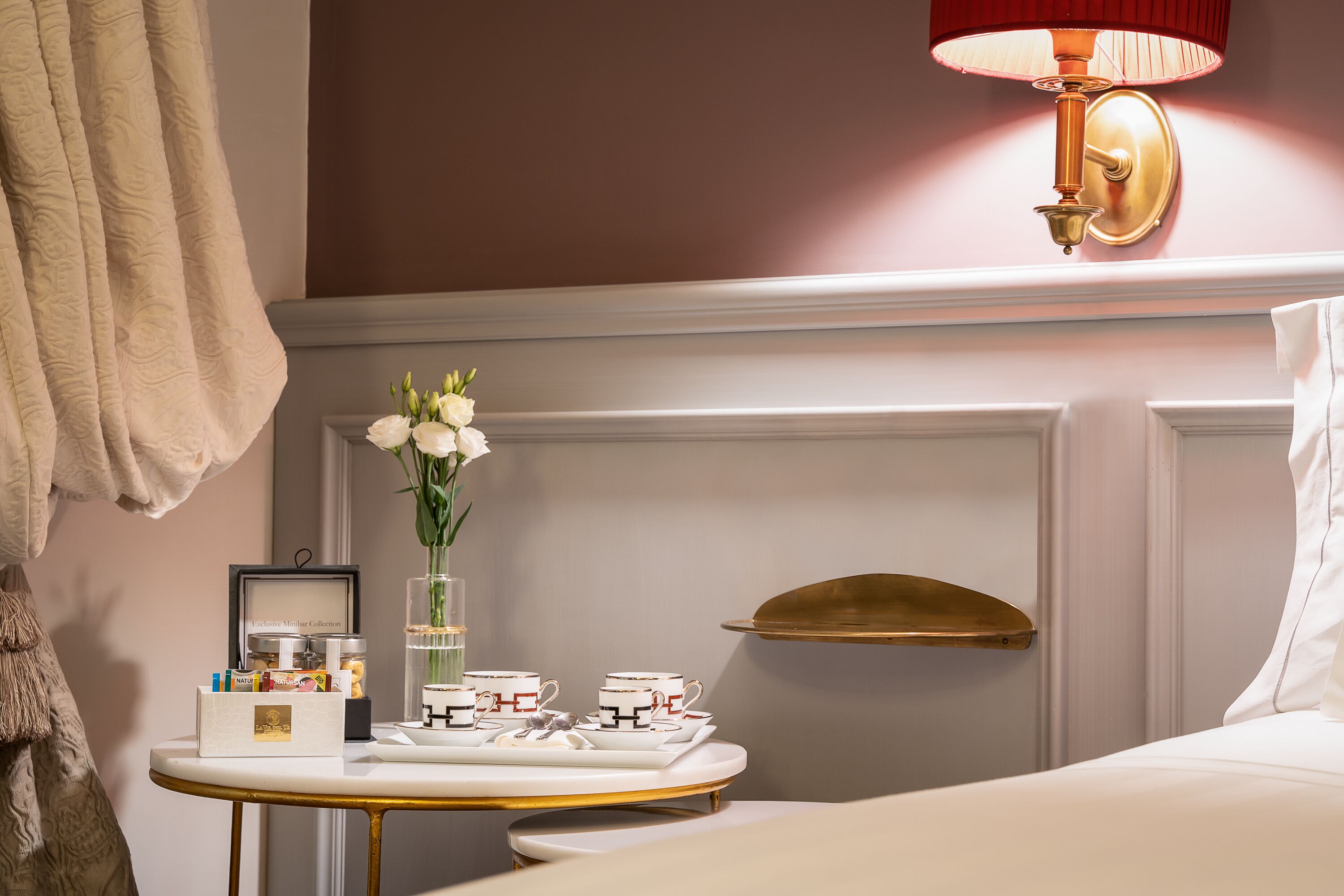 A neatly arranged bedroom with a bedside table holding a tray of tea cups and a vase of flowers.