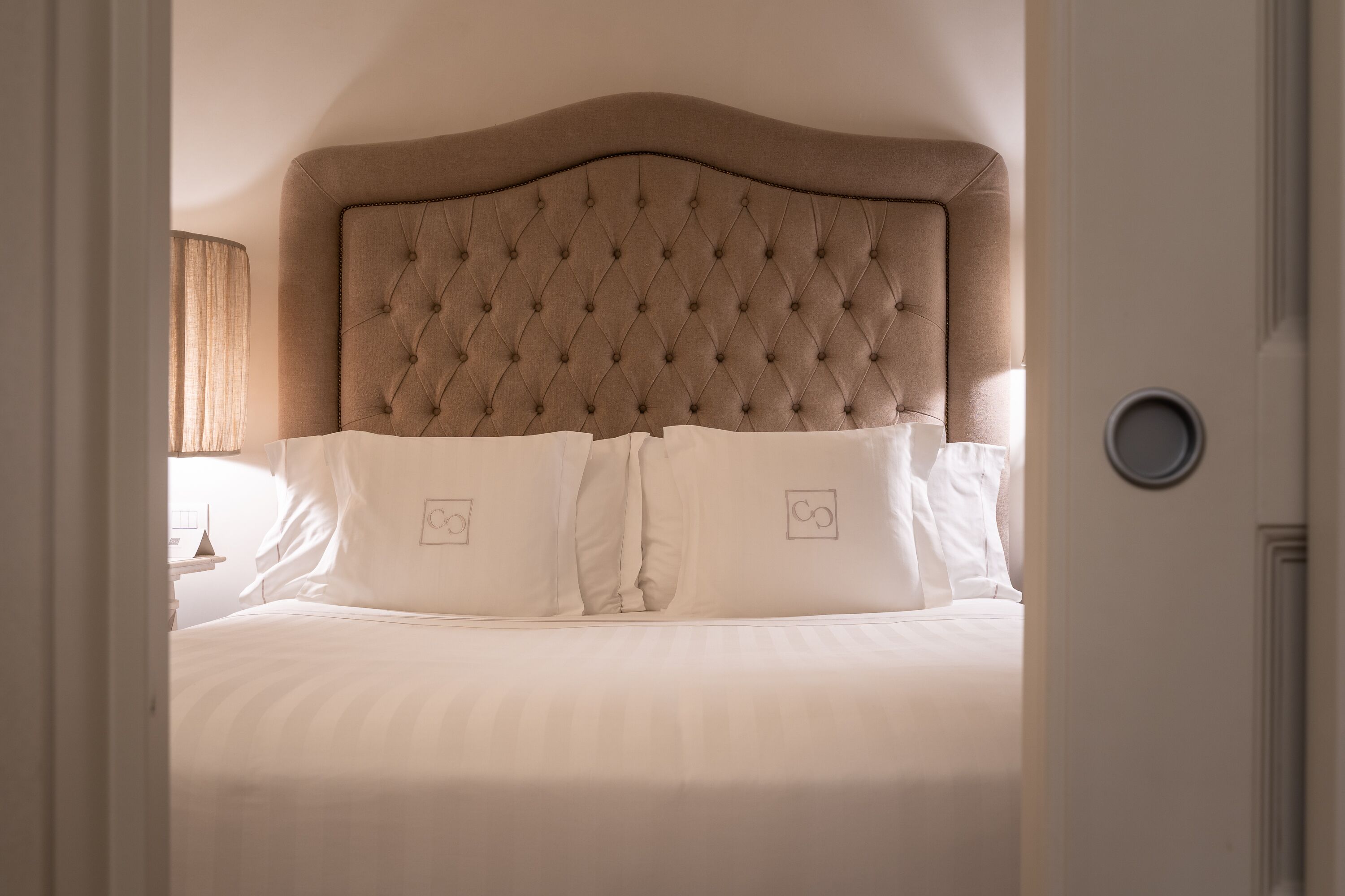 A neatly made bed with a tufted headboard, white bedding, and two pillows with a simple design.