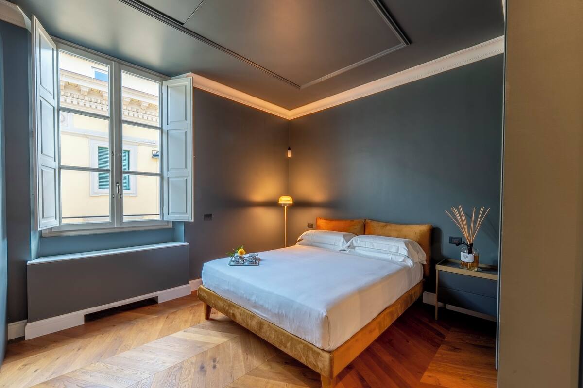 A bedroom with a bed, bedside table, lamp, and window.