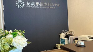 Ein Empfangstresen mit dunkler Wand, einer Blumenkomposition und einem Brother-Drucker.