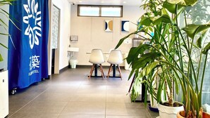 Eine Hotelhalle mit einer Rezeption, zwei Stühlen, Topfpflanzen und einem blauen Vorhang mit einem Logo.