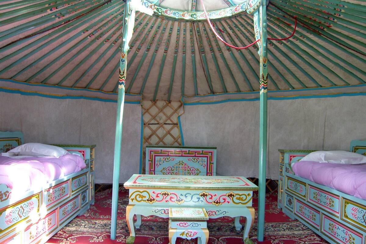 Una yurta tradicional con dos camas, una mesa central y un tapiz decorativo en la pared.