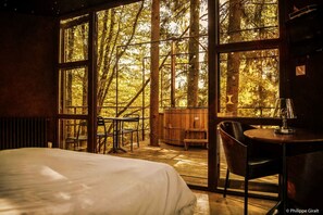 A bedroom with a large window, a bed, a table, and a chair. - Moulin de la Jarousse - Les Cabanes (Angoisse)