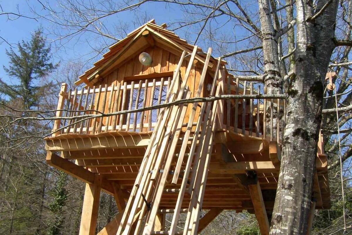 A wooden treehouse with a balcony, surrounded by trees.