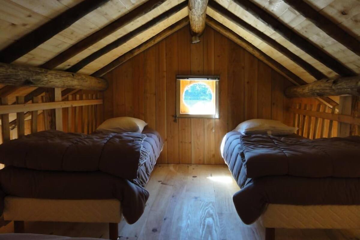 A cozy attic bedroom with two single beds, wooden beams, and a small window.