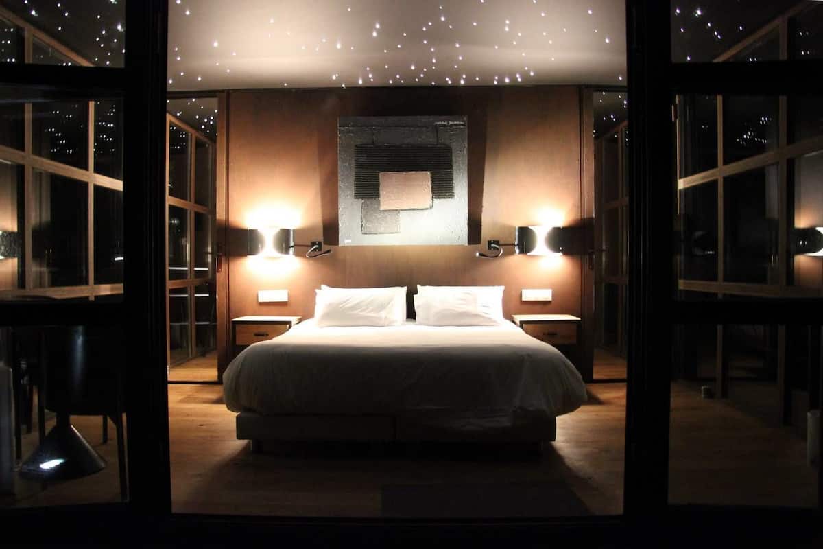 A modern bedroom with a large bed, two bedside tables, and wall-mounted lamps.