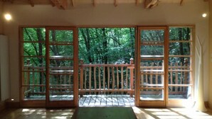 A room with large sliding glass doors leading to a deck, wooden flooring, and a simple table. - Moulin de la Jarousse - Les Cabanes (Angoisse)