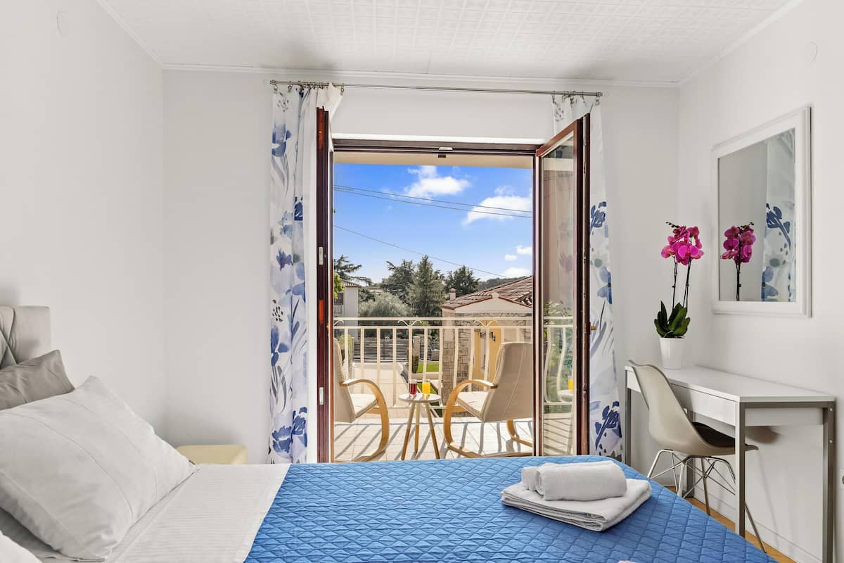 A hotel room with a bed, a desk, a chair, and a balcony with a view of the outside.