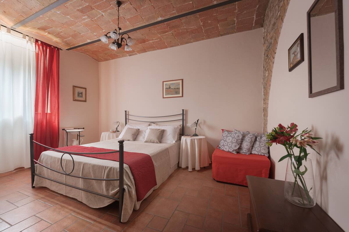 Ein Schlafzimmer mit einem Bett, Nachttischen, einem roten Sofa, einer Blumenvase und einer Ziegeldecke.