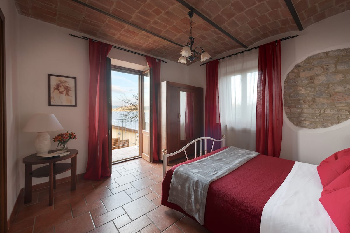 Ein Schlafzimmer mit Bett, Nachttisch, Lampe und Fenster mit roten Vorhängen.
