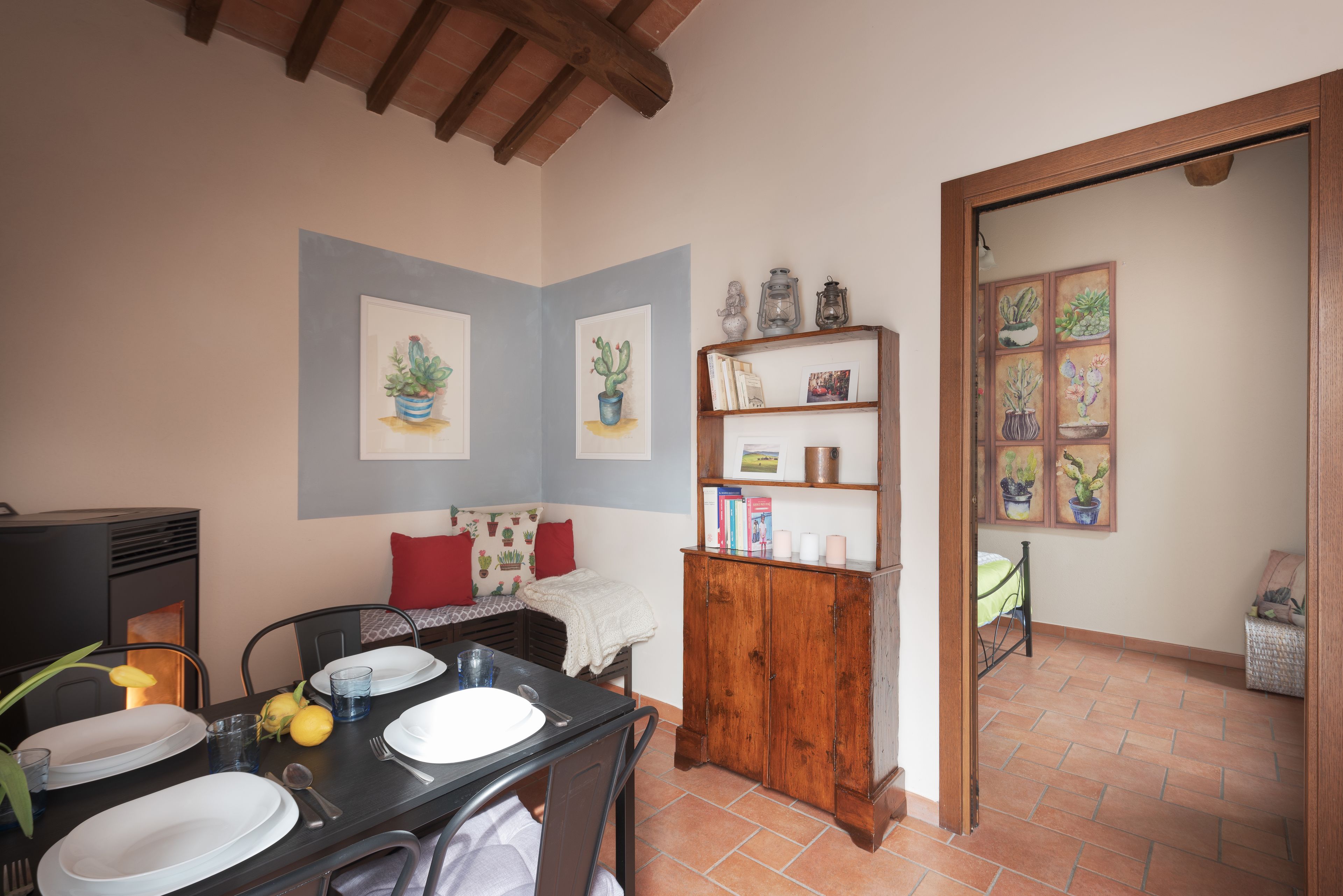 A dining area with a table set for four, a wooden cabinet with books and decorative items, and a wall with framed artwork.