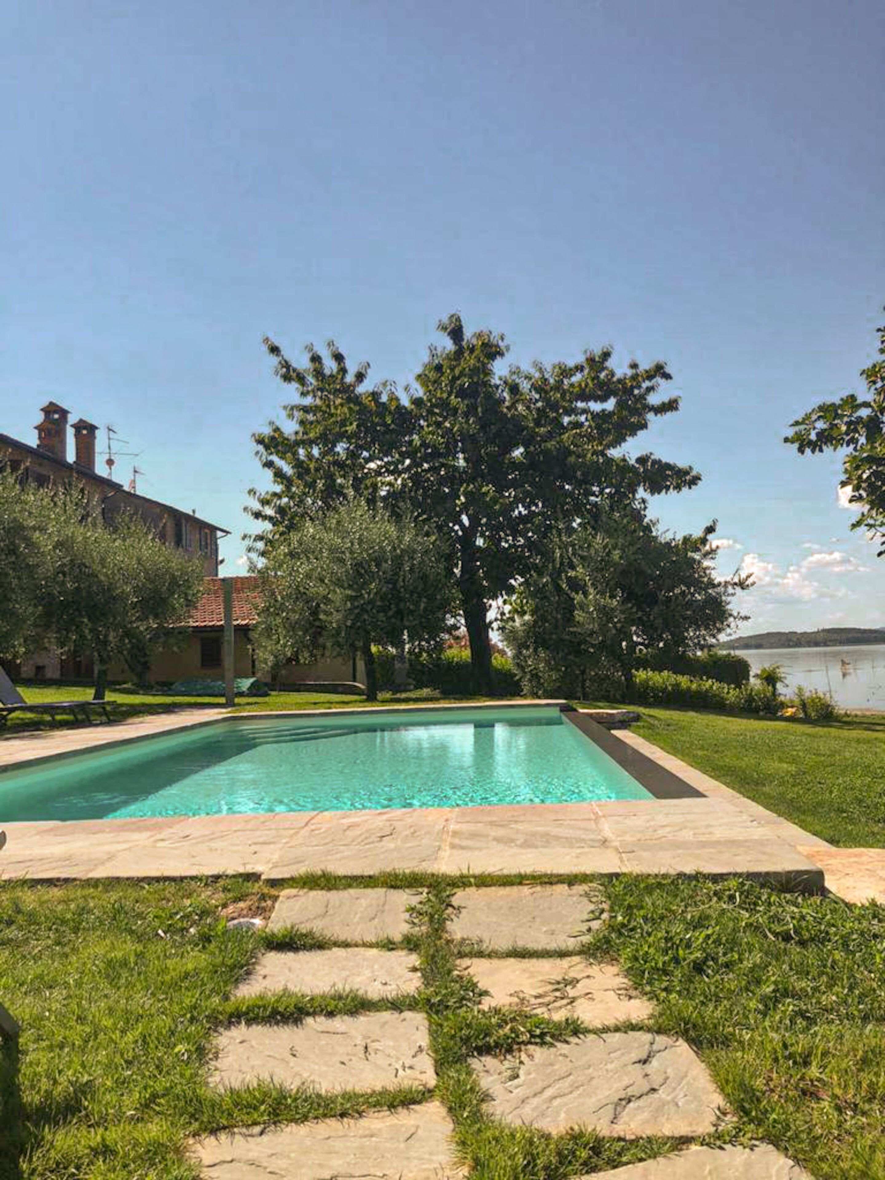 Une piscine bordée d’un chemin de pierre qui y mène, entourée d’herbe et d’arbres.
