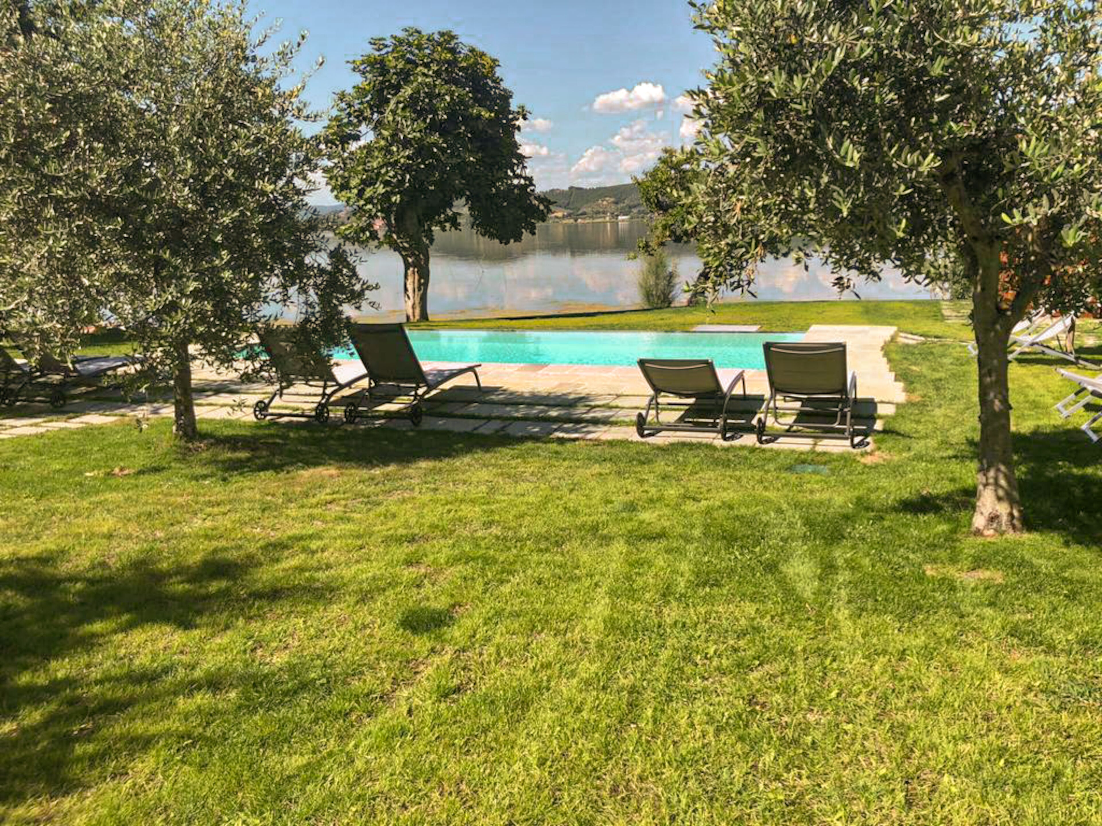 A poolside area with two lounge chairs and a small pool, surrounded by trees and a grassy lawn.