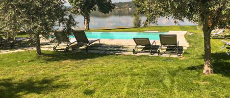 A poolside area with two lounge chairs and a small pool, surrounded by trees and a grassy lawn.