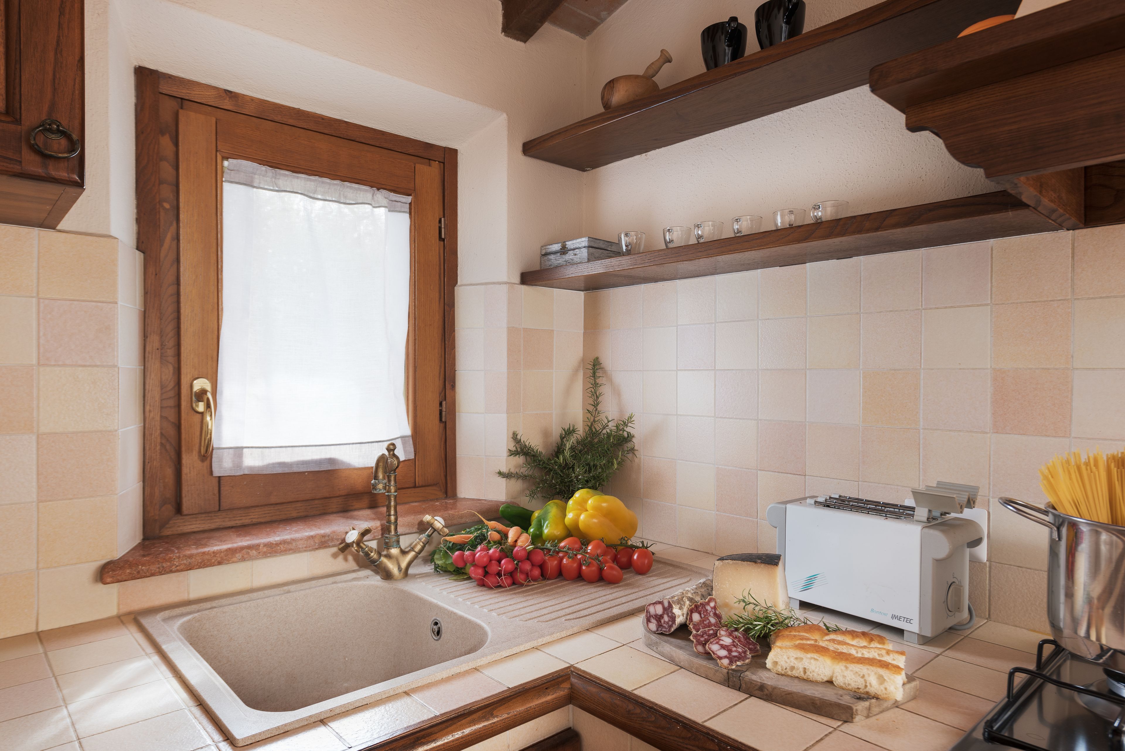 A kitchen with a sink, wooden shelves, a toaster, and various food items.