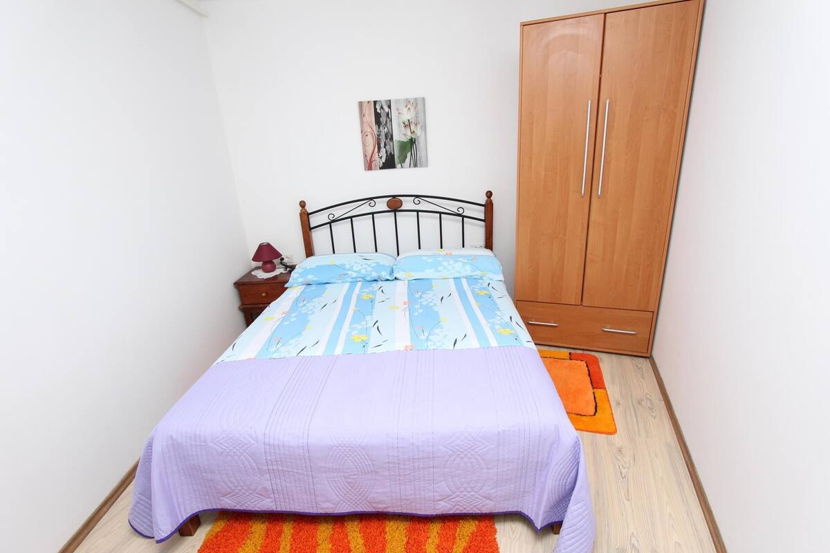 Een slaapkamer met een bed, nachtkastje, kledingkast en een klein schilderij aan de muur.