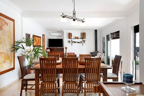 A dining area with a wooden table and chairs, a chandelier, and wall-mounted shelves with decorative items. - Air-Conditioned Villa with Luxurious Pool Area & Terrace Close to Golf Course (Costa Teguise)
