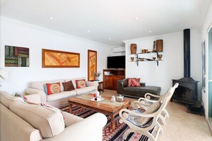 A living room with a sofa, armchairs, a coffee table, a fireplace, and wall-mounted shelves. - Air-Conditioned Villa with Luxurious Pool Area & Terrace Close to Golf Course (Costa Teguise)