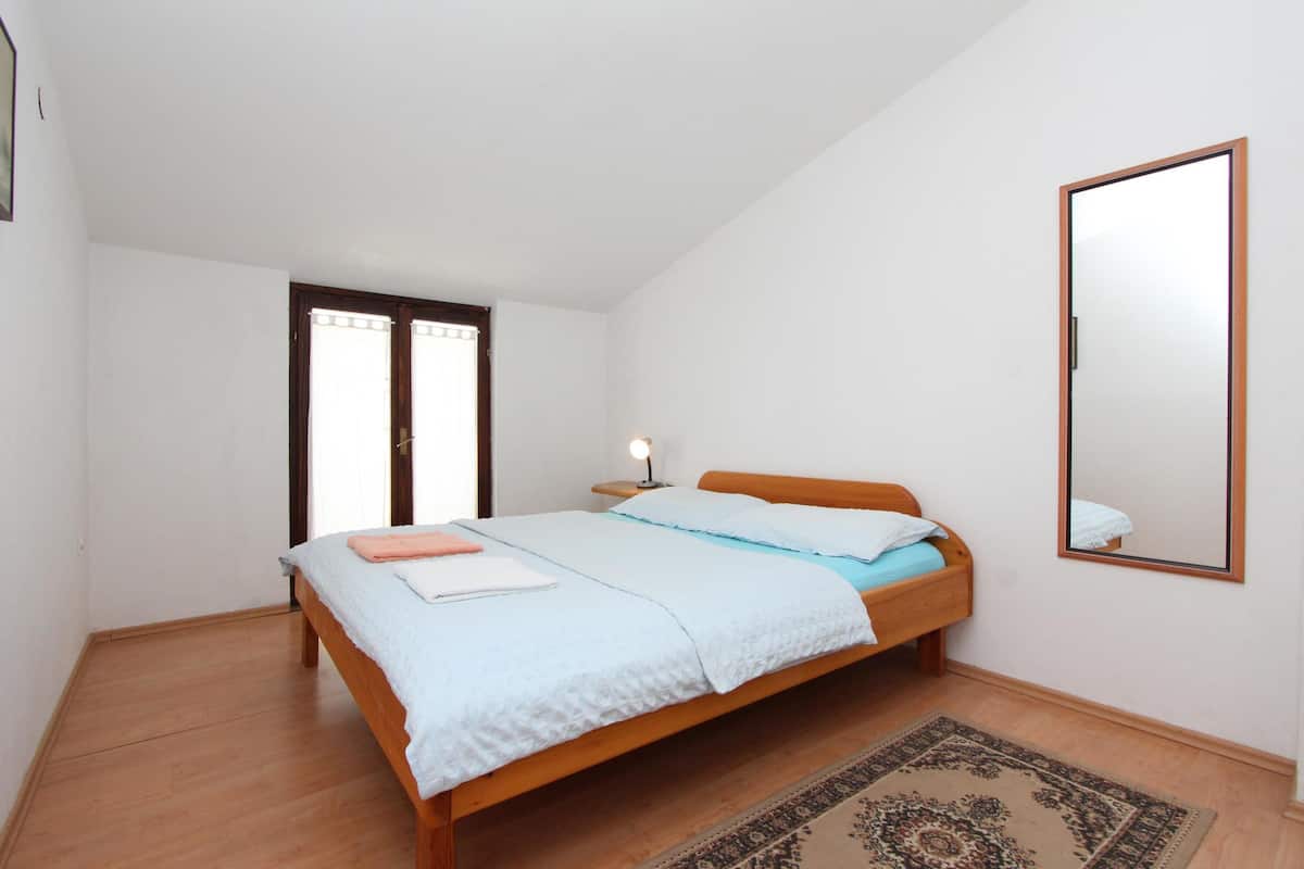 Ein Schlafzimmer mit einem hölzernen Bett, einem Nachttisch mit Lampe, einem großen Spiegel und einem gemusterten Teppich.