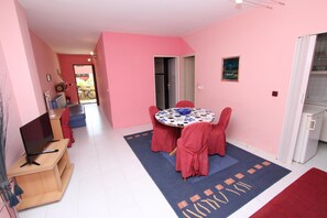 A room with pink walls, a round table with red chairs, a TV on a wooden stand, and a small refrigerator.