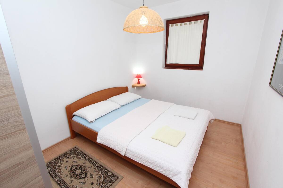 Ein ordentlich bezogenes Bett mit Holz-Kopfstück, einer Nachttischlampe und einem an der Wand befestigten Regal mit Lampe.