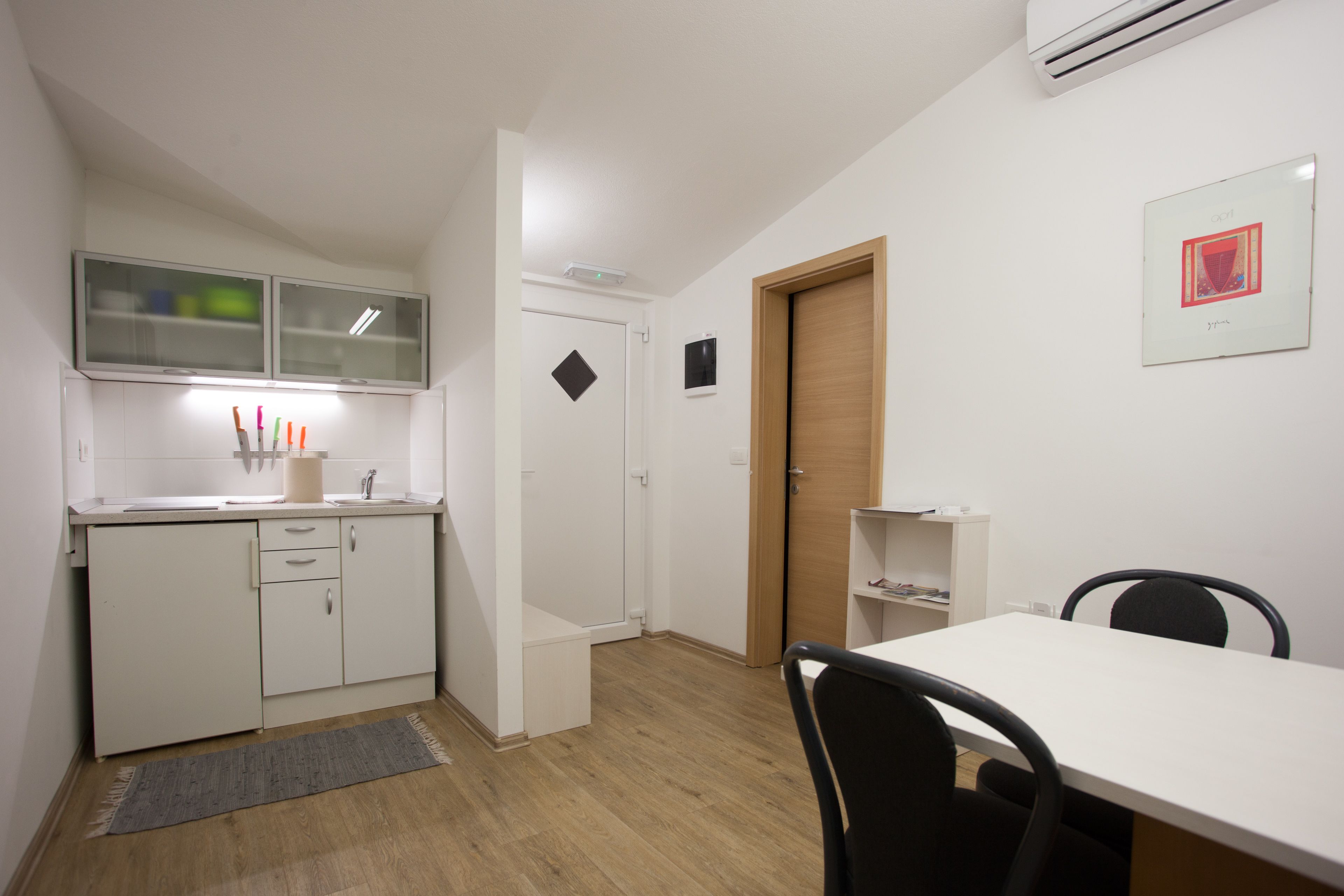 A compact kitchen with white cabinets, a wooden door, and a small dining area with a table and chairs.