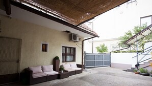 A covered outdoor seating area with a sofa and a small table, a gate, and a staircase leading to an upper level. - Apartments SHISHKA (Ljubljana)