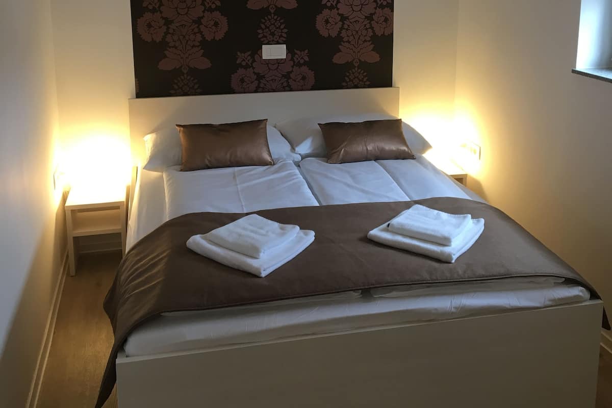 Een hotelkamer met een groot bed, twee nachtkastjes met lampen, een donker hoofdbord met bloemendesign en een raam aan de rechterkant.