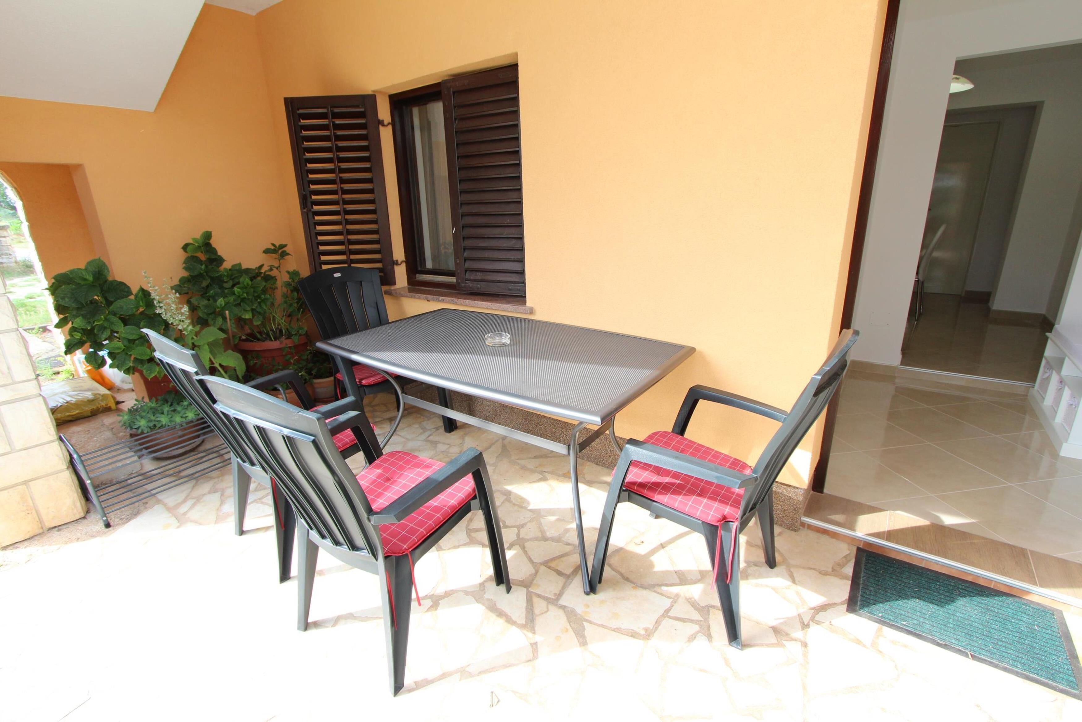 An outdoor patio with a table and chairs, potted plants, and a view of the interior.