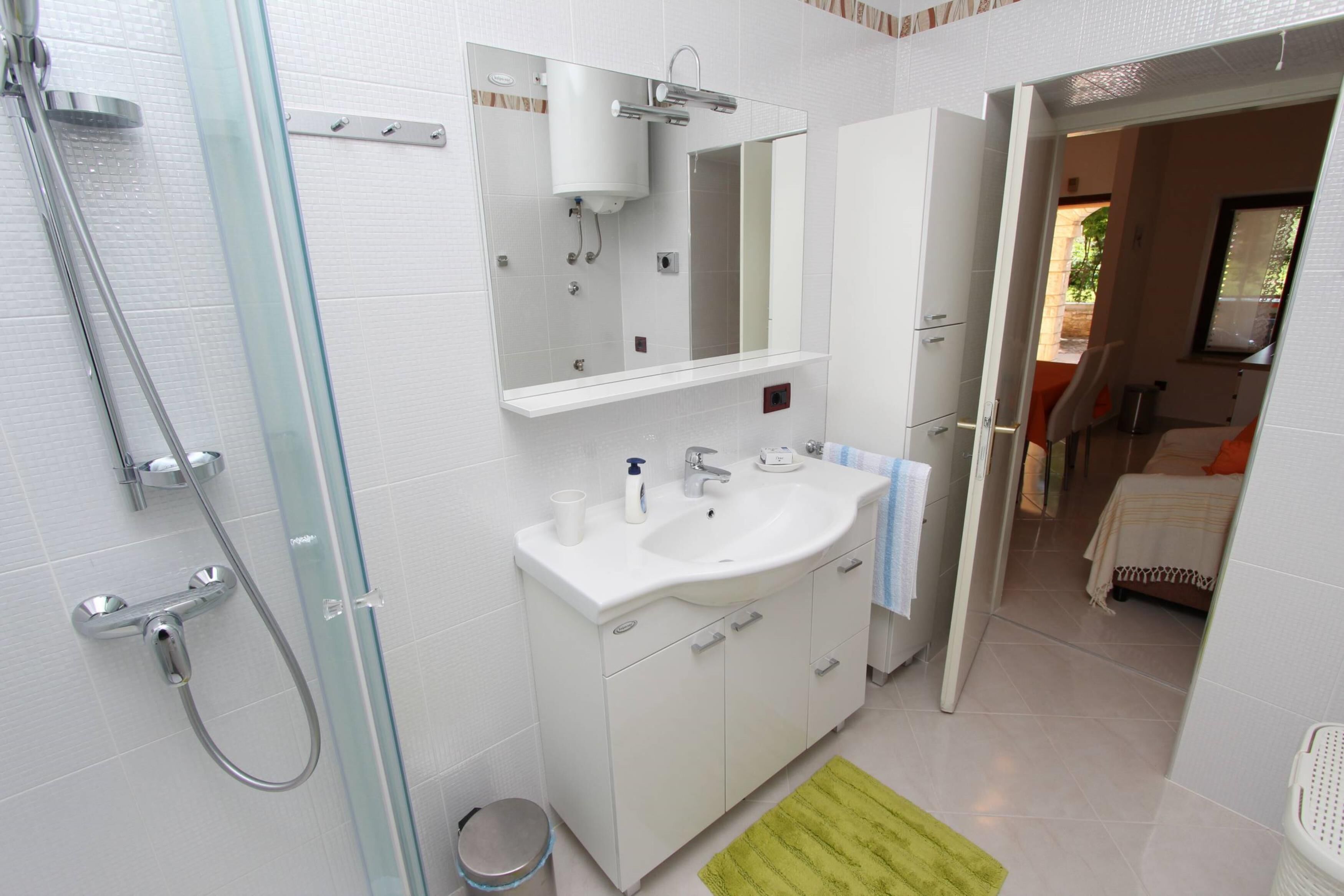 Un bany modern amb plat de dutxa de vidre, un lavabo blanc i un mirall al damunt.