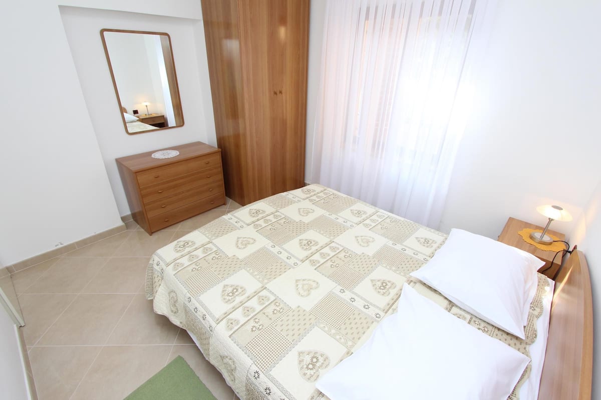 Une chambre à coucher avec un lit, une commode en bois, un miroir et une table de chevet avec une lampe.