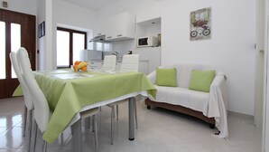 A modern kitchen with white cabinets, a microwave, and a dining area with a green tablecloth and white chairs.