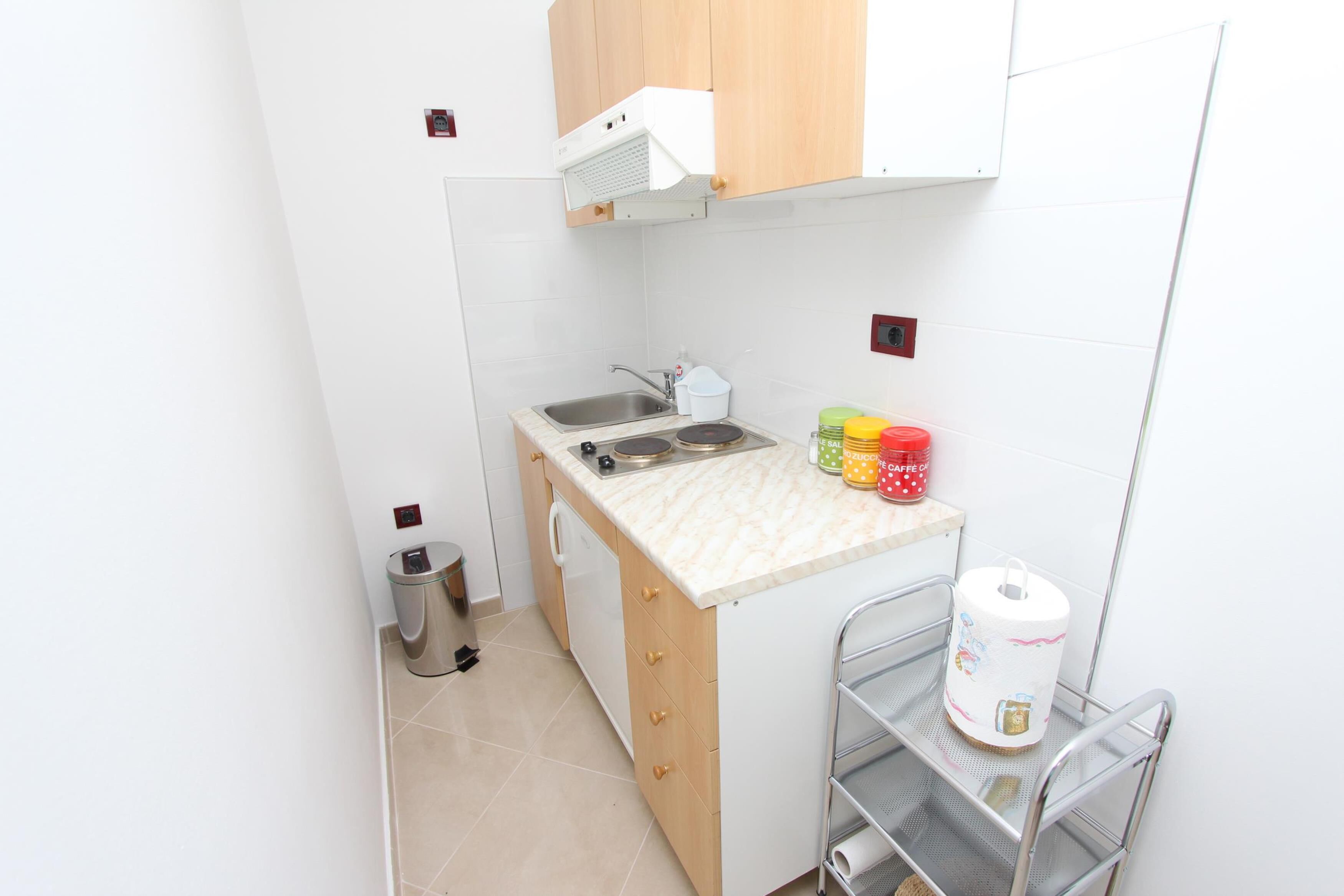 Una pequeña kitchenette con lavamanos, estufa y armarios de almacenamiento.