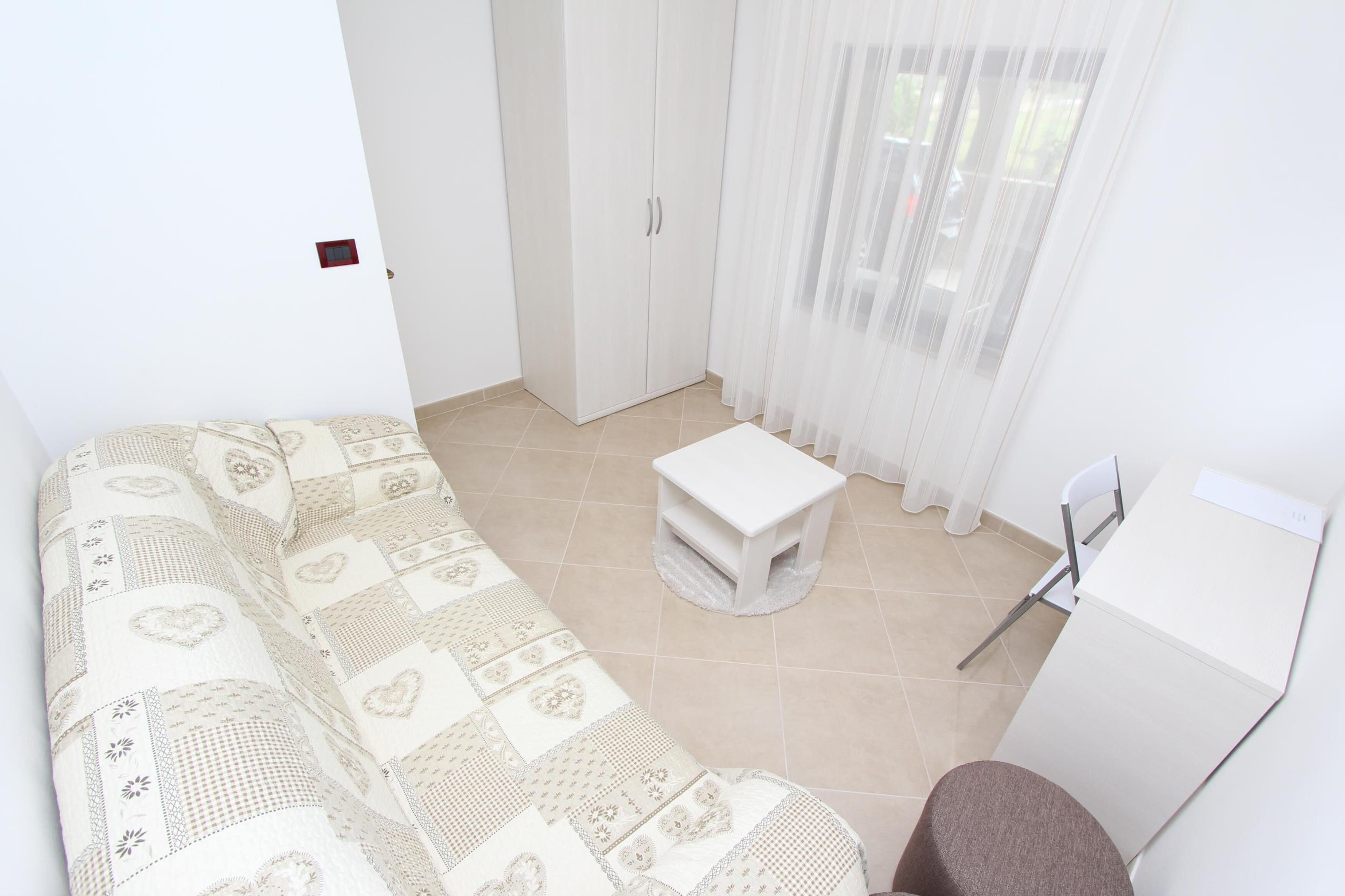 A small, clean room with a patterned sofa, a small table, a chair, and a wardrobe.