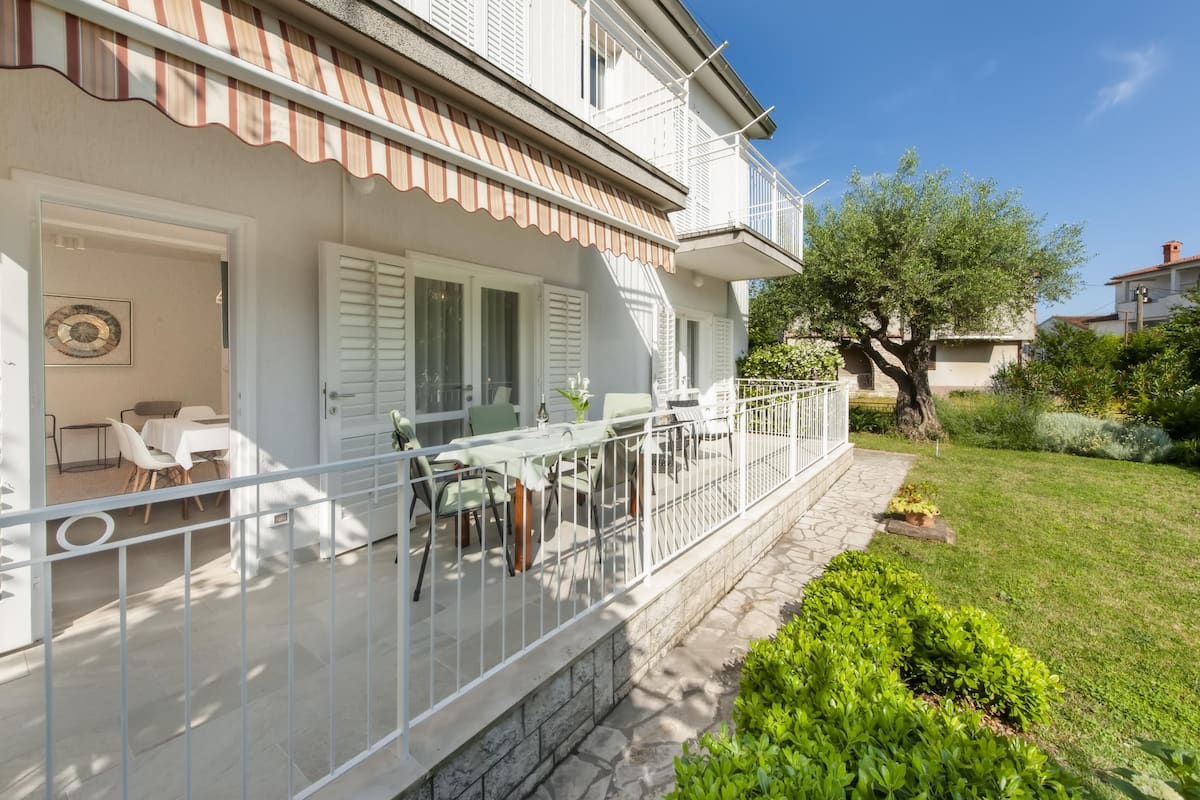 Uma casa de dois andares com varanda coberta, mobiliário de exterior e um jardim bem cuidado.