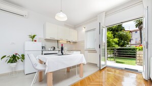 Una cocina moderna con armarios blancos, una mesa de comedor con sillas y un ventanal corredero que da a un balcón con vistas a zonas verdes y edificios.